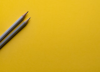 two gray pencils on yellow surface