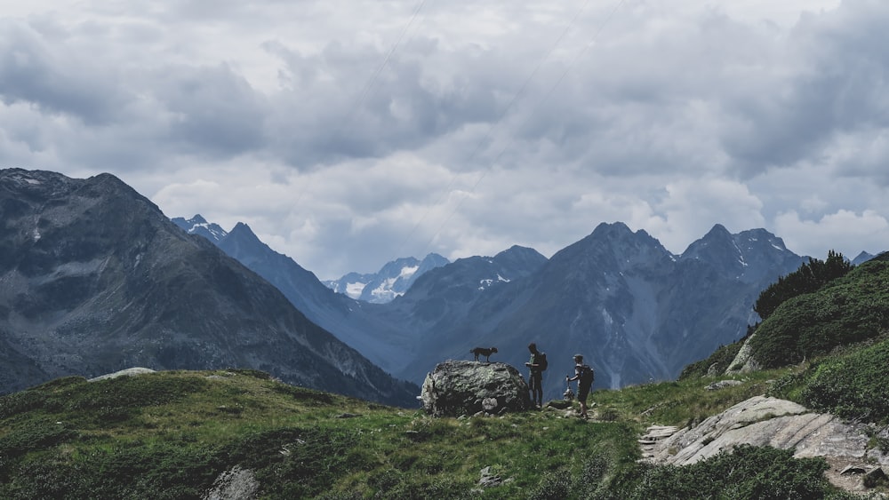 personne debout sur le champ d’herbe verte près de la montagne sous les nuages blancs pendant la journée