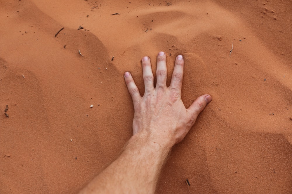 A person placing their hand on sand.