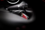 A close-up view of a Mini car key fob inserted in the ignition, with blurred surrounding elements of the car's interior. The key fob has a shiny, red surface with several buttons.