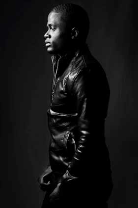 a sharply dressed male model wearing a dark, premium leather jacket with intense cinematic lighting on a black background