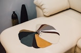 A selection of fabric swatches on a beige leather couch, with various colors fanned out. Two decorative vases are visible in the background, placed against a neutral-colored wall.