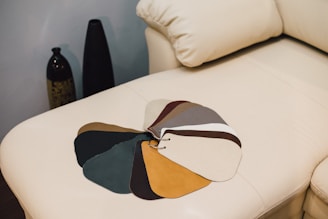 A selection of fabric swatches on a beige leather couch, with various colors fanned out. Two decorative vases are visible in the background, placed against a neutral-colored wall.