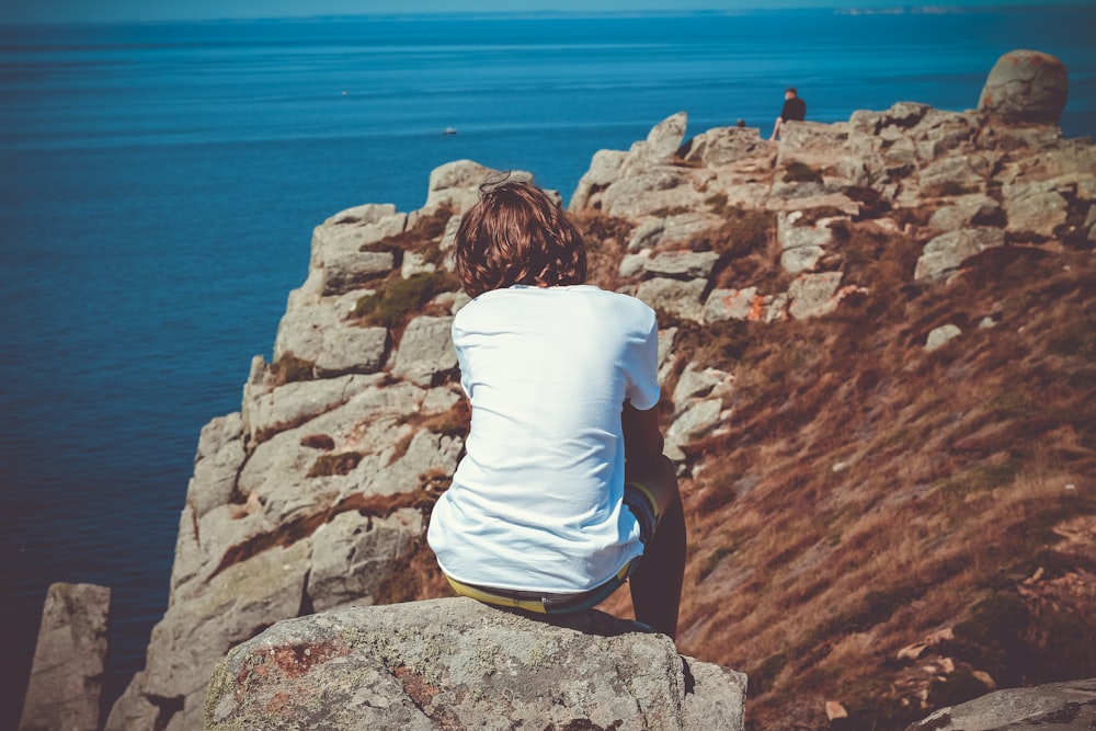 a person sitting on top of a rock near the ocean