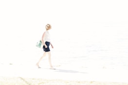 A happy person carrying a Sunshell Bag along a sunny boardwalk, with the sea sparkling behind them.