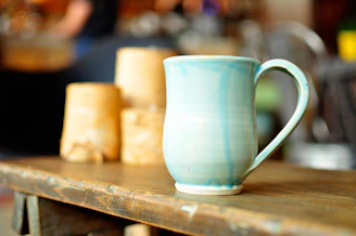 A vibrant hand-thrown ceramic mug with swirling blue and yellow glazes resting on a wooden table.