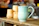A close-up of a bright blue hand-thrown ceramic mug resting on a wooden table with soft morning light.
