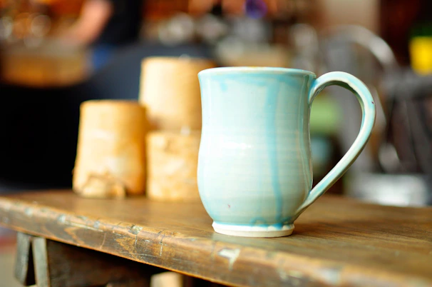 A vibrant hand-thrown ceramic mug with swirling blue and yellow glazes resting on a wooden table.