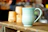 A close-up of a bright blue hand-thrown ceramic mug resting on a wooden table with soft morning light.