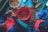 Two people are seated at a table covered in pecan shells. They are wearing blue and red clothing. One person appears to be cracking pecans while the other is sorting them. Several containers are scattered on the table, with a large red bowl in the center filled with broken shells.