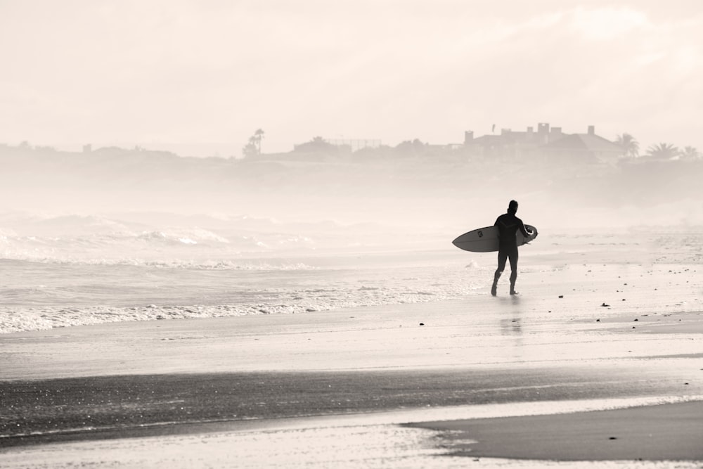 silhouette person walking on sandbank while holding surfboard