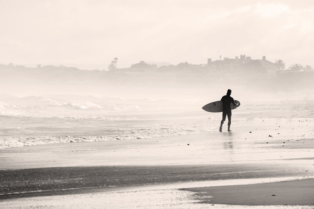 Silueta de persona caminando en el banco de arena mientras sostiene la tabla de surf