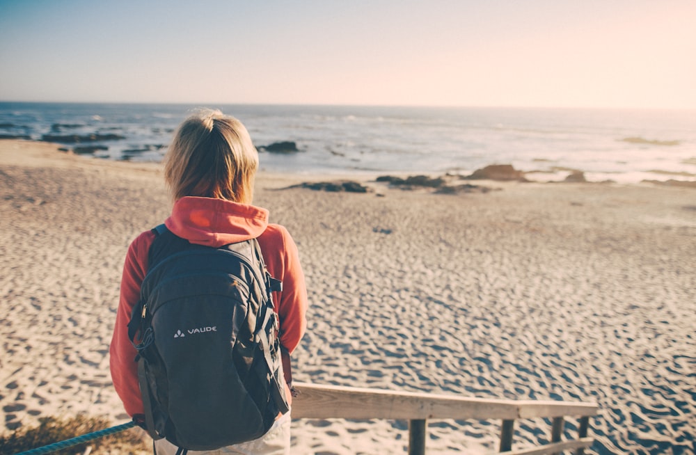 woman in black and red hoodie standing on beach during daytime