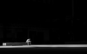 grayscale photogaphy of man sitting on concrete bench