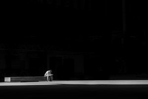 grayscale photogaphy of man sitting on concrete bench