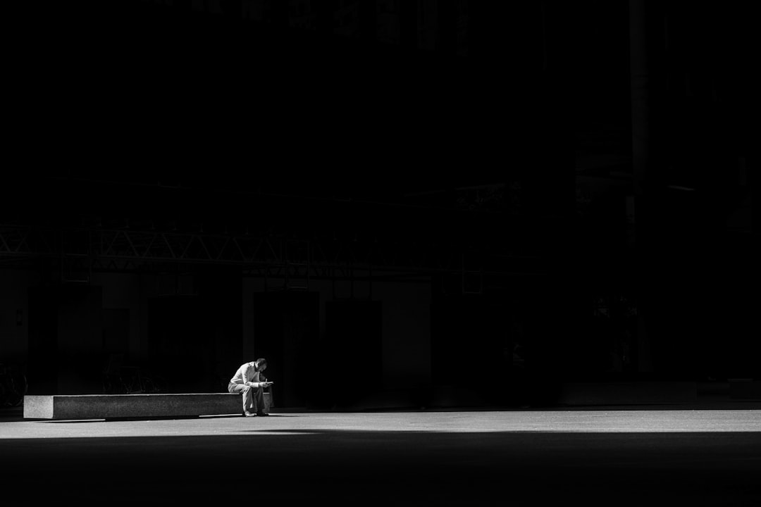 grayscale photogaphy of man sitting on concrete bench,