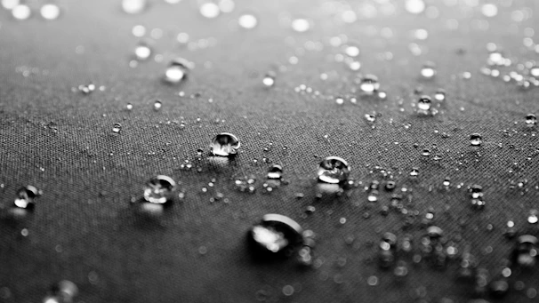 Close-up of a waterproof fabric sample with water droplets beading on the surface.