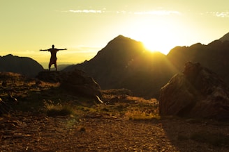 A model wearing a featherlite hiking vest standing on a rocky outcrop during sunset.