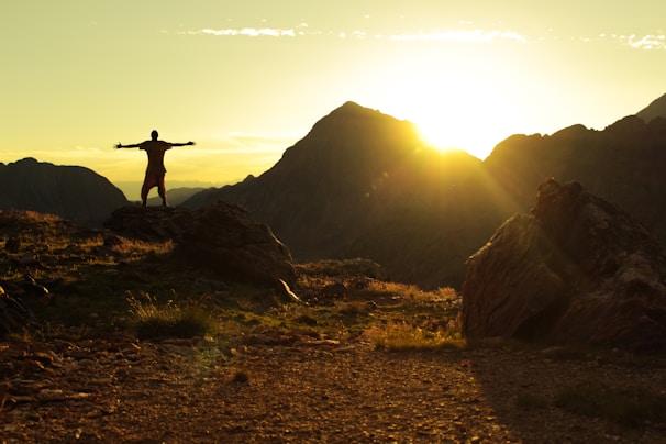 A model wearing a featherlite hiking vest standing on a rocky outcrop during sunset.