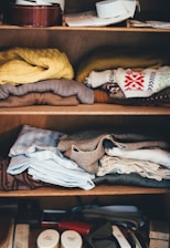 Neatly folded clothes stacked on a wooden shelf in a tidy room.