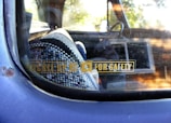 A close-up view of a car window with a safety reminder sticker that reads 'Buckle Up For Safety'. Inside the vehicle, a patterned woven seat cover is visible, along with a portion of the steering wheel. The window shows some wear and has a reflective surface.
