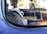 A close-up view of a car window with a safety reminder sticker that reads 'Buckle Up For Safety'. Inside the vehicle, a patterned woven seat cover is visible, along with a portion of the steering wheel. The window shows some wear and has a reflective surface.