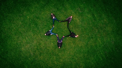 five people laying on grass field making star sign