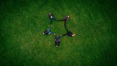 five people laying on grass field making star sign