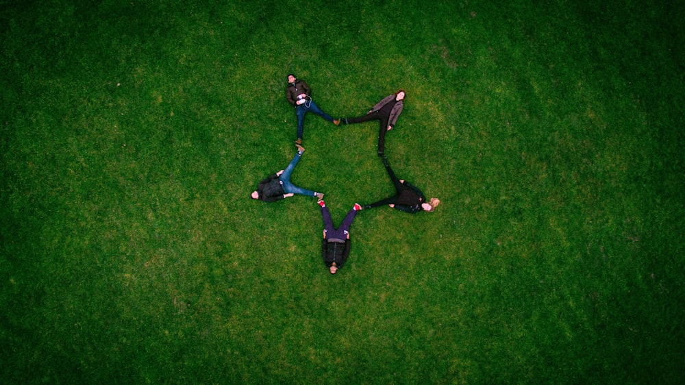 five people laying on grass field making star sign