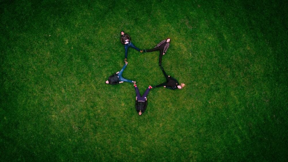 cinq personnes allongées sur le champ d’herbe faisant un signe astrologique