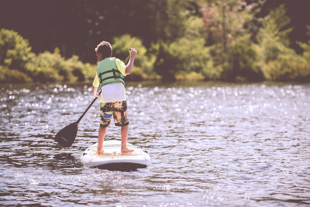 boy riding on surfboard holding black boat oats during daytime