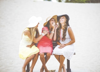 three women sitting on brown wooden bench