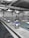 A spacious indoor swimming pool area with multiple lanes marked by black and white flags. Diving platforms are numbered and positioned at the pool's edge. The space is industrial with exposed piping and large lighting above. The walls have abstract line patterns and the overall setting is tidy and quiet.