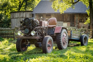 A compact Tordis trailer filled with farming tools, parked beside a tractor in a sunny field.