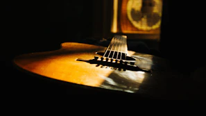 Close-up of a vintage guitar resting on a wooden floor with soft sunlight streaming in.