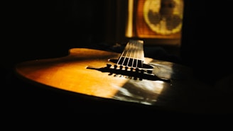 A wooden acoustic guitar is resting with light streaming onto its surface, casting warm shadows. The focus is on the body and strings of the guitar, creating a serene and intimate atmosphere.