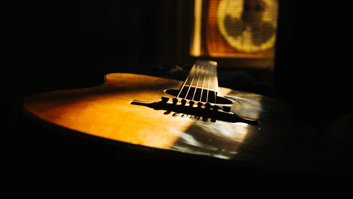 Close-up of a vintage acoustic guitar resting against a worn wooden chair in soft natural light