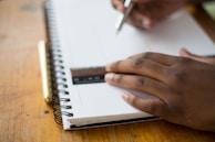 person holding ruler and pencil on spiral notebook