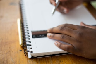 person holding ruler and pencil on spiral notebook
