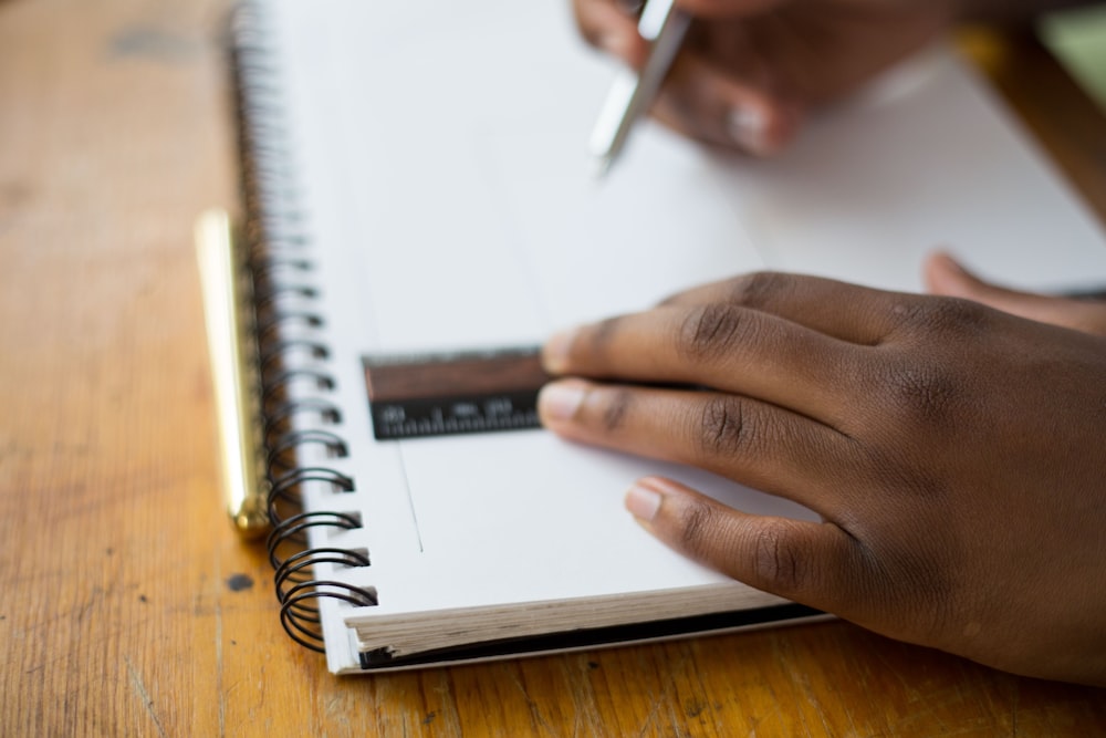 person holding ruler and pencil on spiral notebook