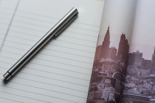 A sleek gold pen resting on a black leather-bound financial report with London skyscrapers blurred in the background.