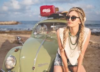 selective focus photography of woman sitting on Volkswagen Beetle parked on beach shore
