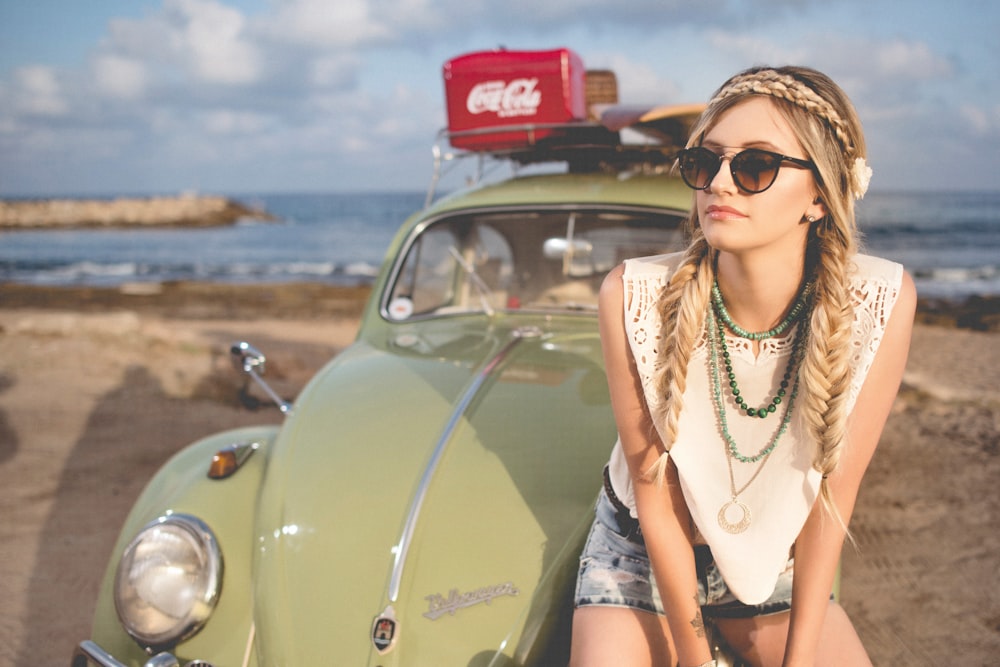selective focus photography of woman sitting on Volkswagen Beetle parked on beach shore