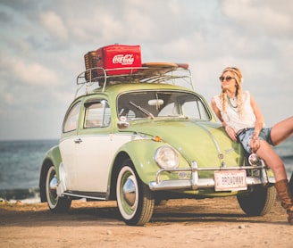 woman leaning on green and white Volkswagen Beetle near sea under white sky during daytime