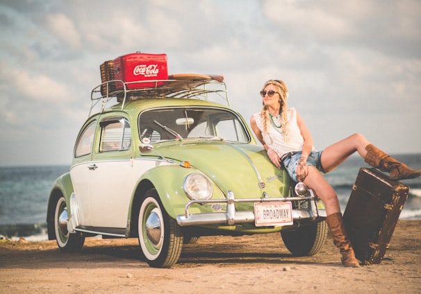 woman leaning on green and white Volkswagen Beetle near sea under white sky during daytime