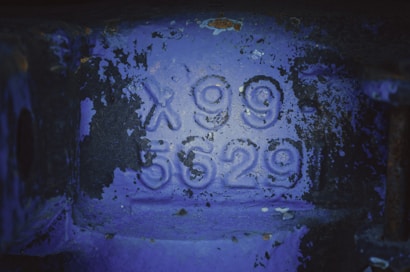 Metallic surface with rust and paint peeling, showing embossed characters X99 5629 in the center.