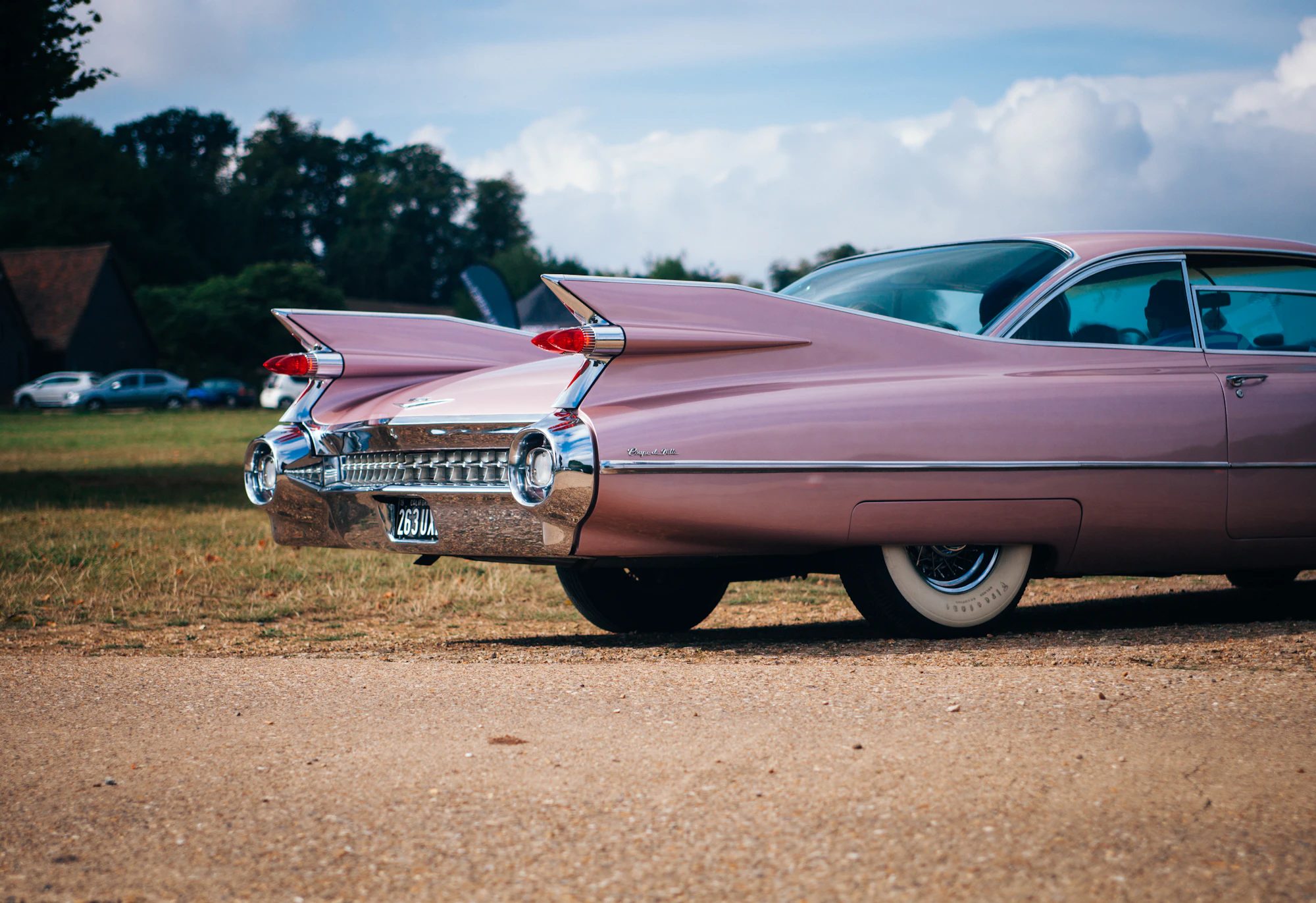A pink vintage car parked beside a field