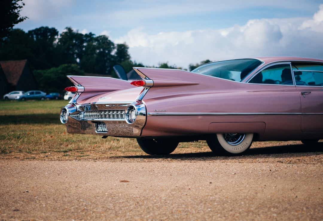 vintage pink muscle car parked near field of grass,