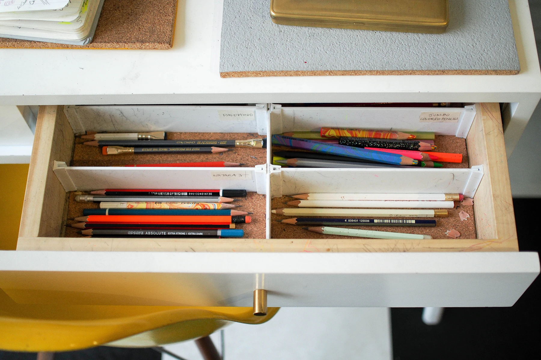 An open desk drawer of pencils sorted into labeled compartments
