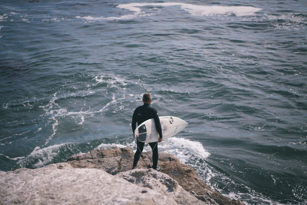 hombre sosteniendo una tabla de surf de pie frente al mar